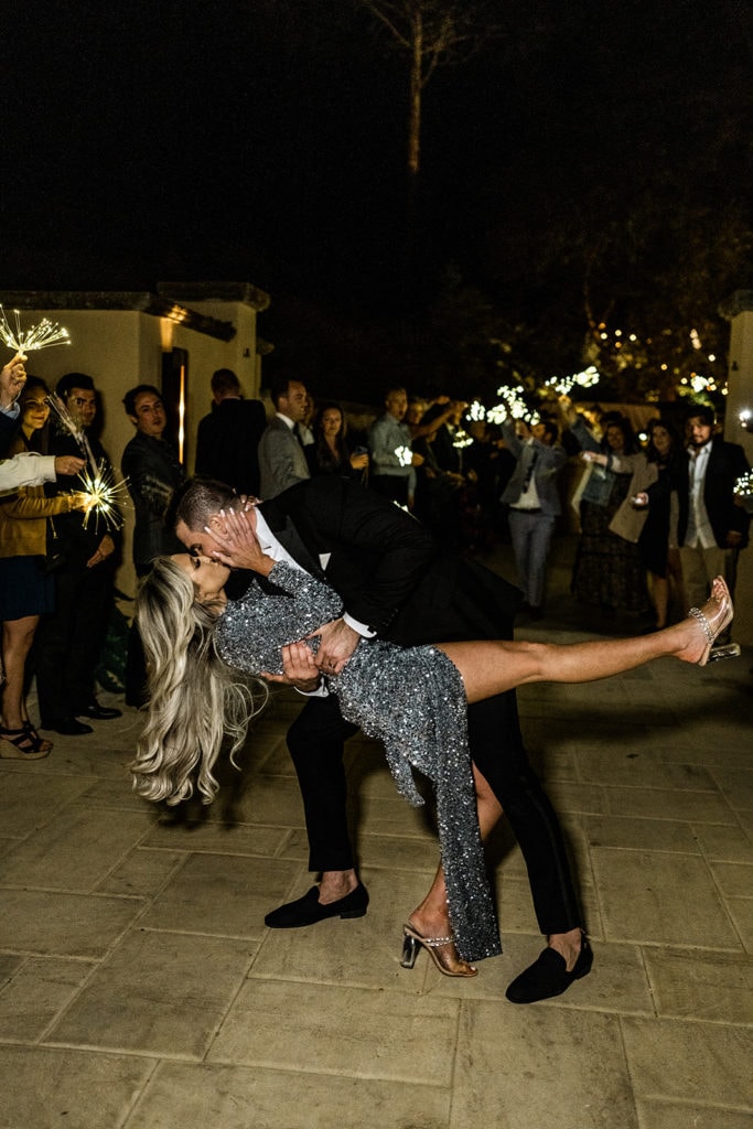 A groom dips his bride and kisses her during a sparkler grand exit. 