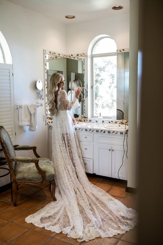 A bride stands before a vanity mirror in a bridal robe from Le Laurier before her Calistoga Vineyard Estate wedding. 