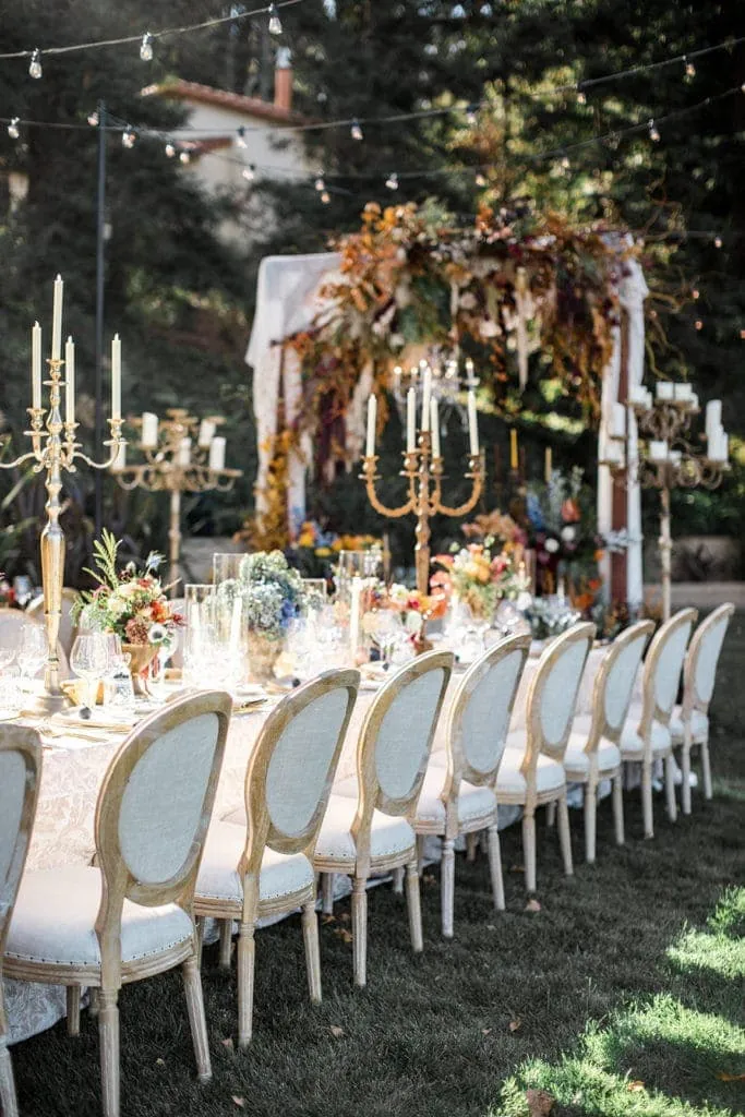 Chairs line a large banquet-style table  which is styled with large, whimsical candelabras and colorful floral centerpieces. 