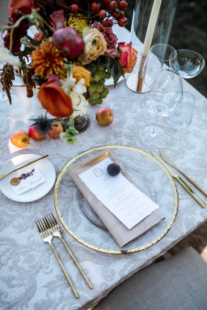 A table setting with a gold rimmed plate and gold dinnerware greet guests at a wedding reception. 