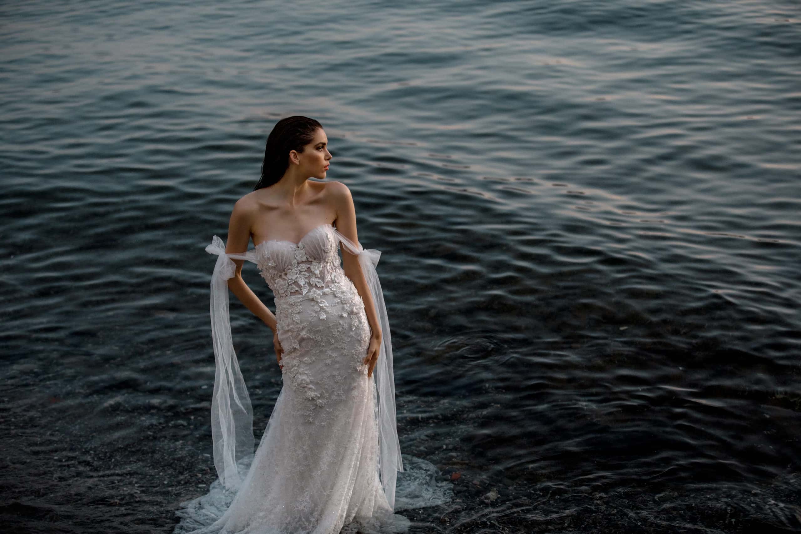 Model stands in Lake Como waters wearing mermaid style, detailed bridal gown