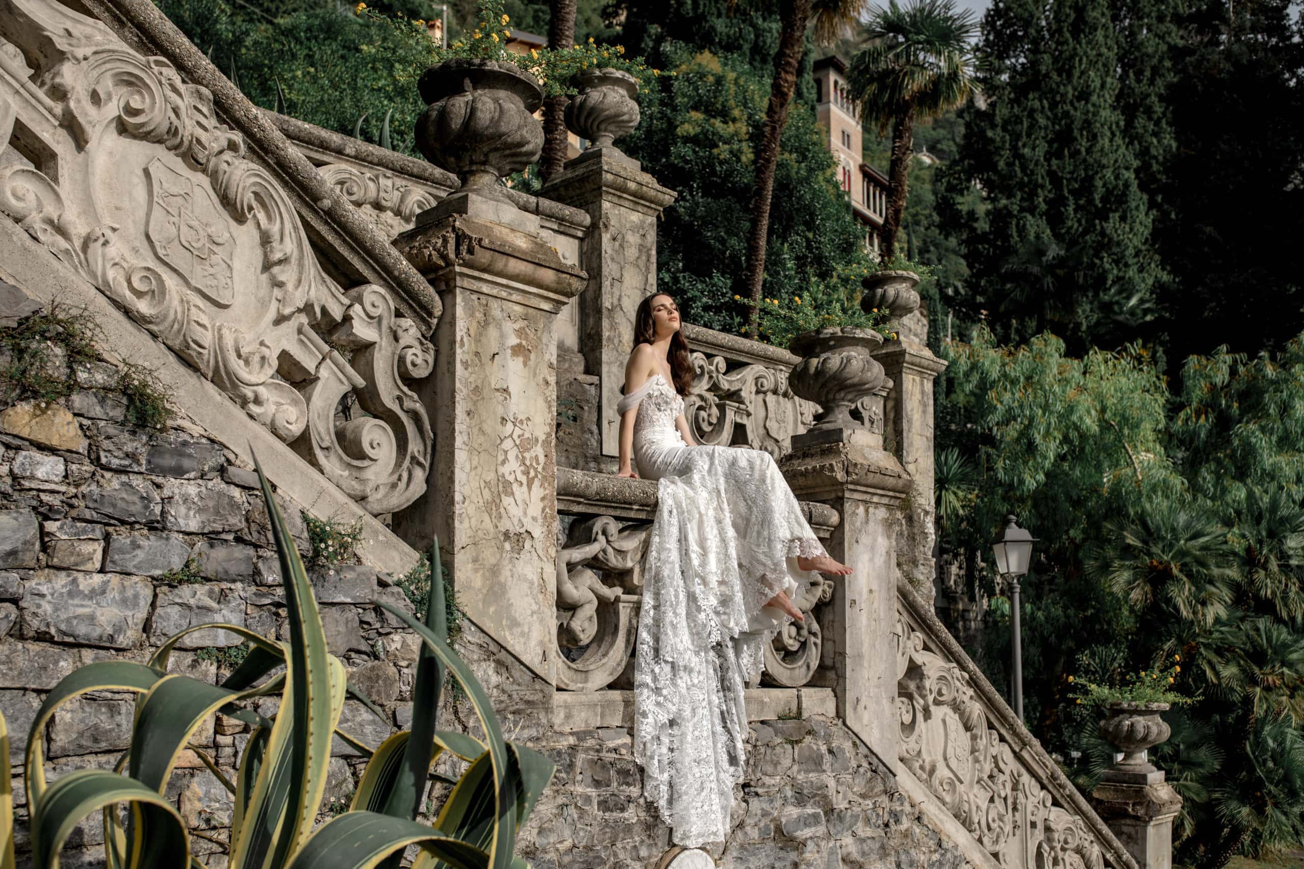 Model sits on banister at Villa Monastero in lace bridal gown