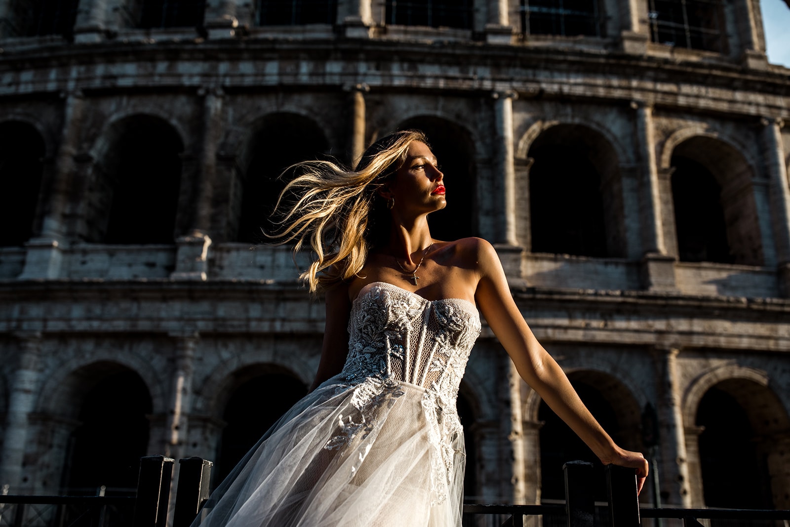 A model bride wearing a wedding gown stands before the Coliseum in Rome