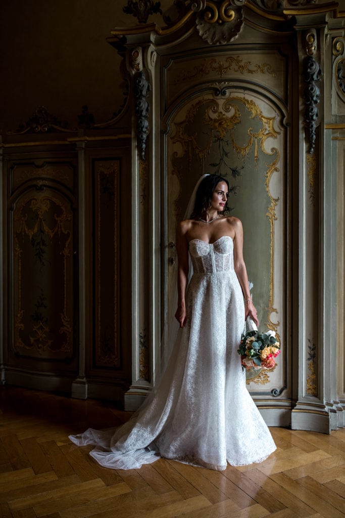 Bride stands before ornate wall in halls of Villa Erba Lake Como.