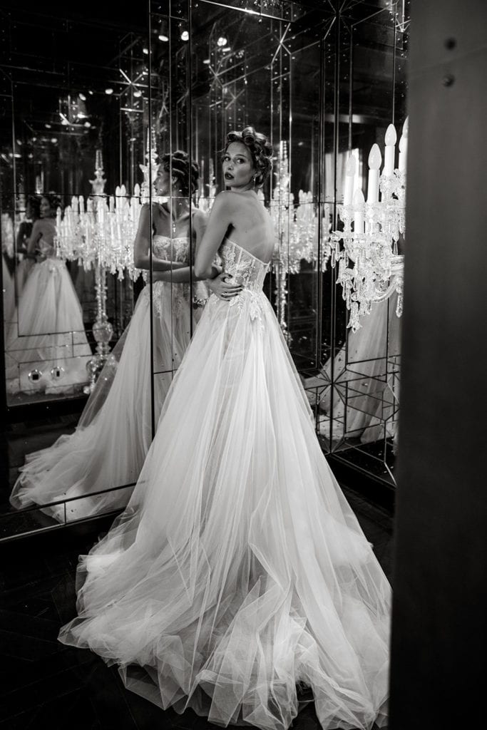 A model bride wearing a Berta wedding gown stands before a wall of mirrors
