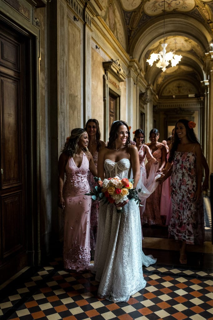 Bride in Berta wedding gown walks with her bridesmaids in the halls of Italian wedding venue