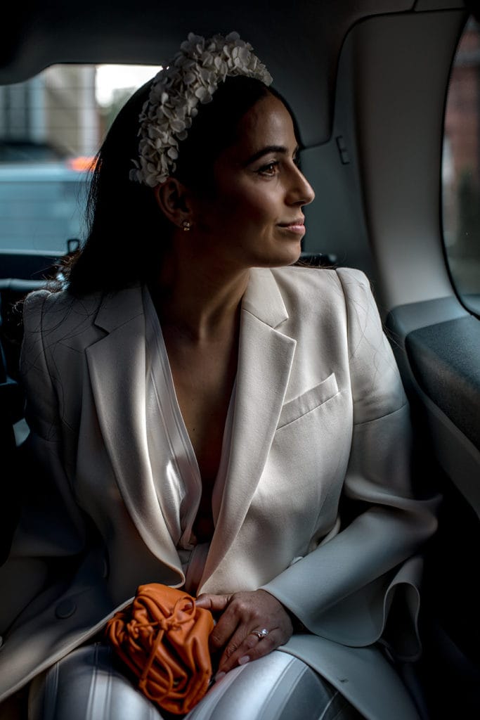 Bride wearing Galvan jumpsuit and floral headband rides in back of a car in London