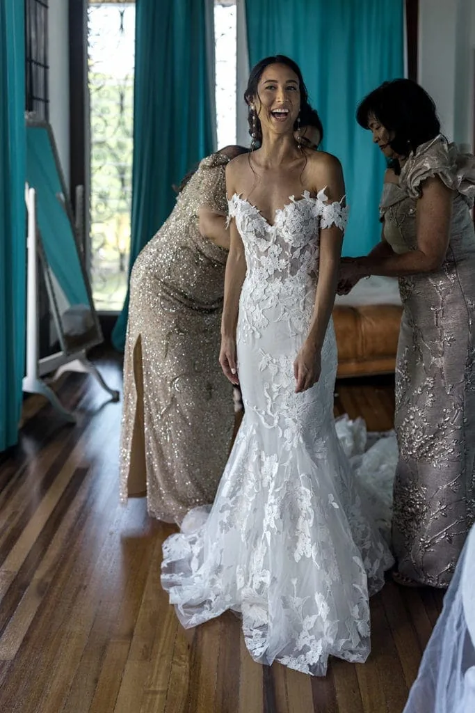 A bride in a Monique Lhuillier wedding gown gets help from her mother and mother-in-law