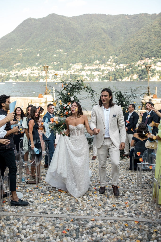 Bride and groom, who wears groom wedding attire ideas, walk down the aisle in Lake Como after just getting married