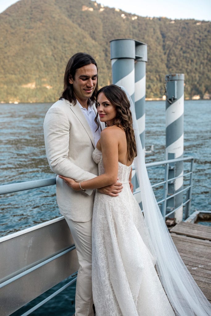 Bride and groom stand together on dock at Lake Como