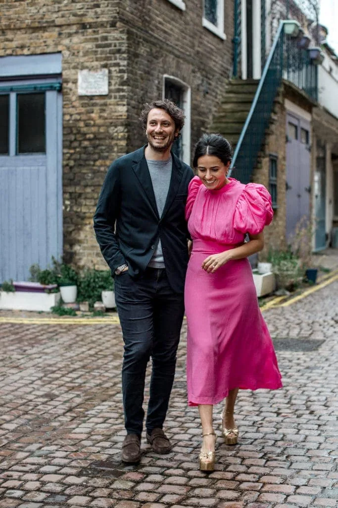 Bride in a bright pink dress and groom walk down streets of London day before their elopement. 