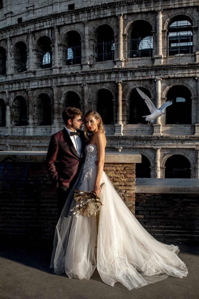 A model bride and groom stand together in front of the Coliseum in Rome