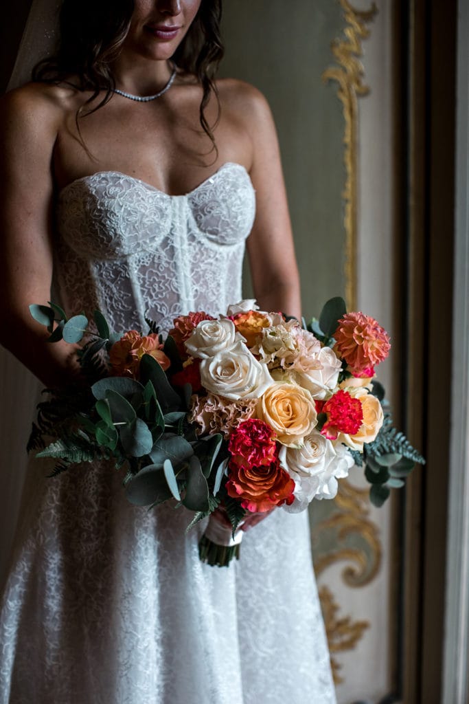 Bride in Berta wedding gown holds a bouquet of red, pink, yellow, and cream colored roses