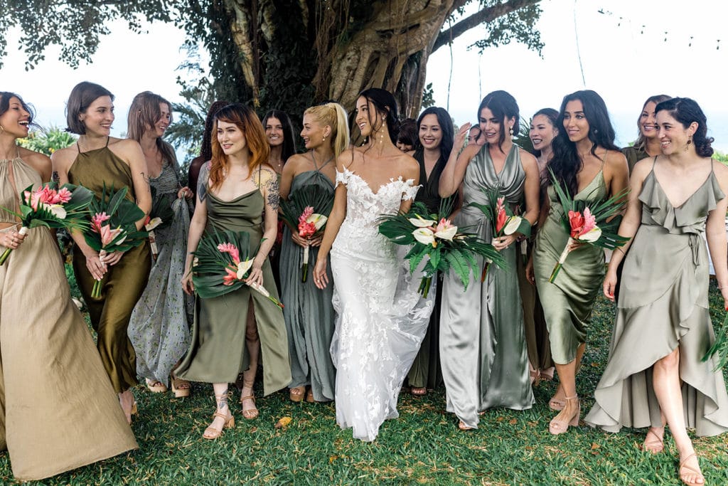 A bride walks with her bridesmaids who are dressed in different shades of green dresses