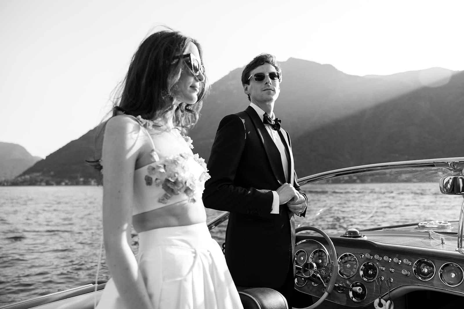 Bride and groom stand on a wooden boat in Lake Como