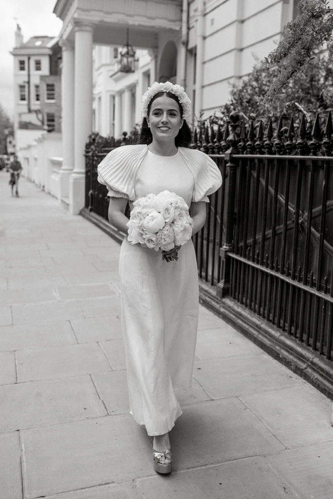 Bride walks down the street carrying peony bouquet before her London elopement ceremony