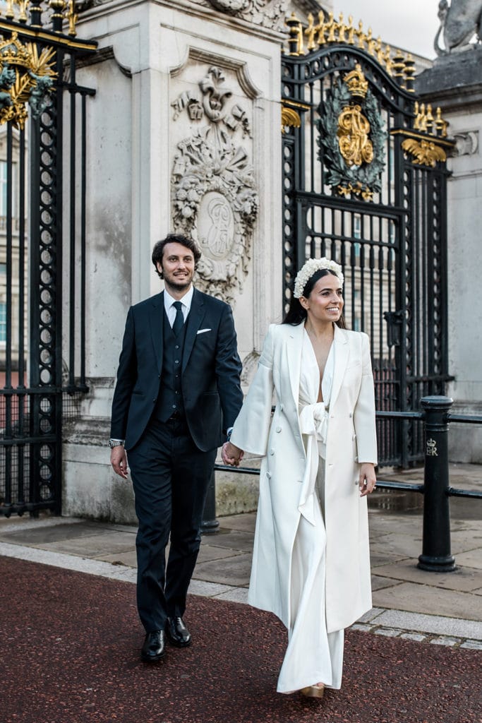 Bride wearing Galvan jumpsuit walks with husband in front of traditional London iron gate