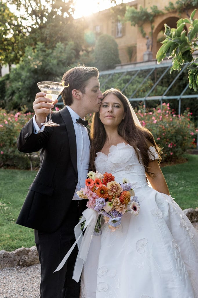 Groom, wearing black tuxedo after finding black tuxedo ideas, toasts the bride during Lake Como sunset portraits