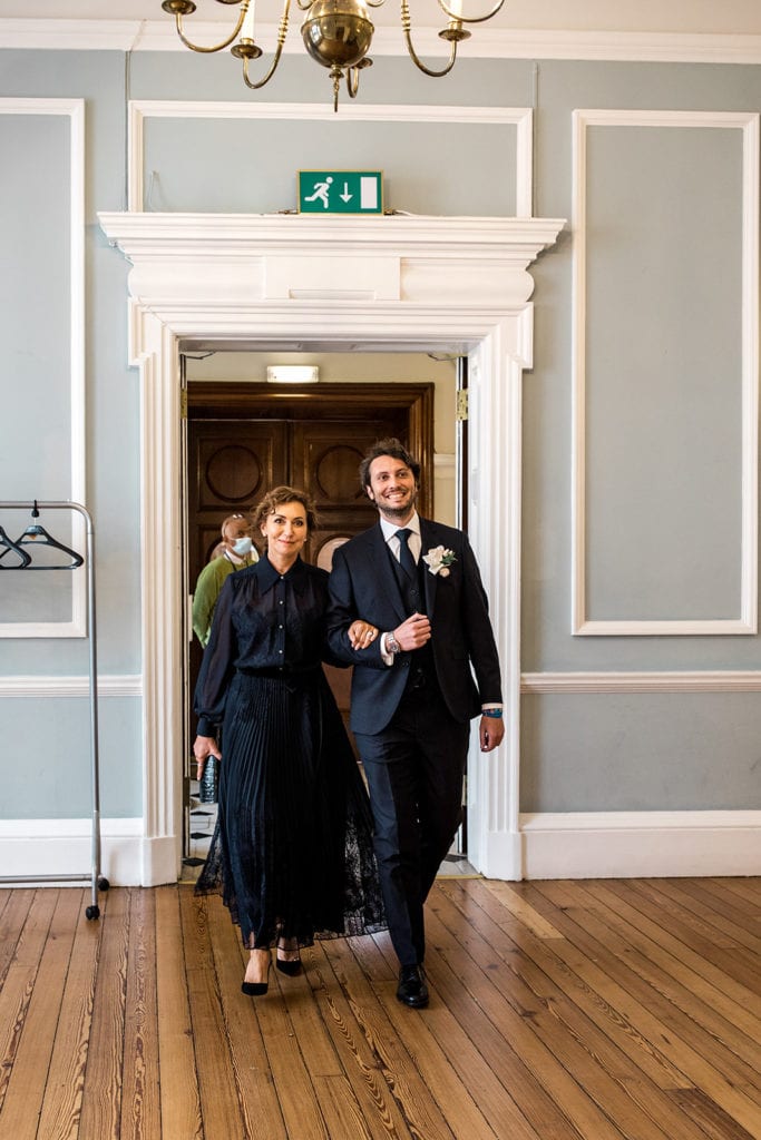 Groom walks with mother in Chelsea Old Town Hall before elopement ceremony