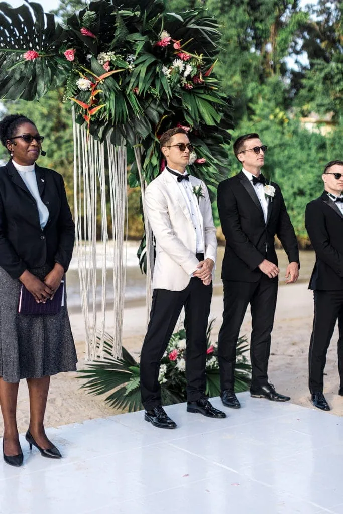 Groom, groomsmen, and the officiant stand at the altar before a beach wedding in Jamaica