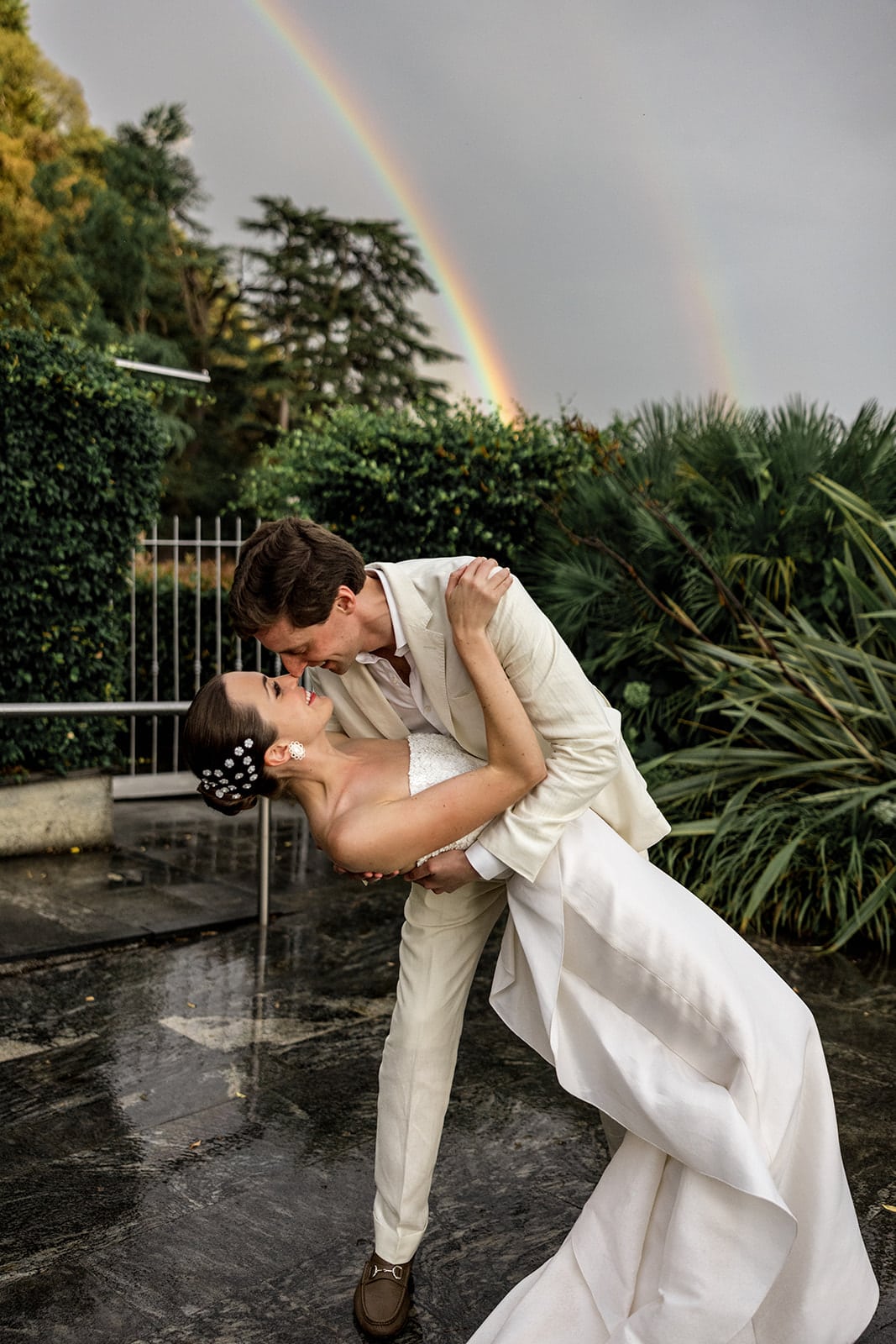 Groom dips bride with a bright rainbow in the background