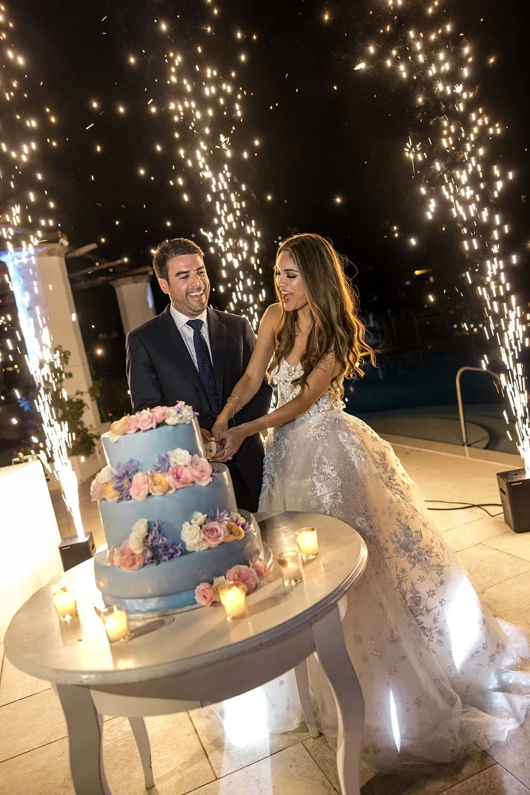 Bride and groom cut the cake with fireworks in background