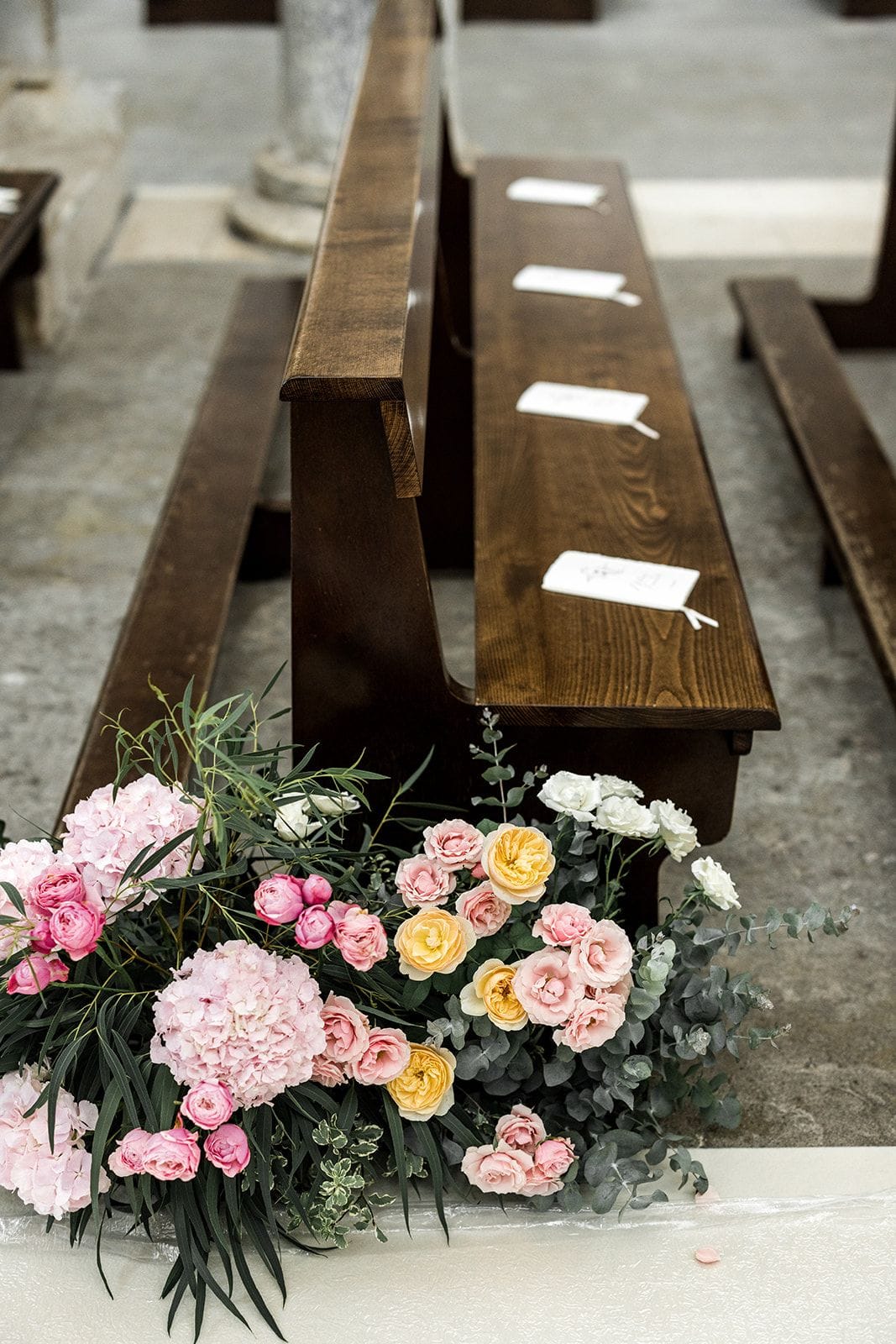 Pink and yellow flowers next to church pew for wedding ceremony