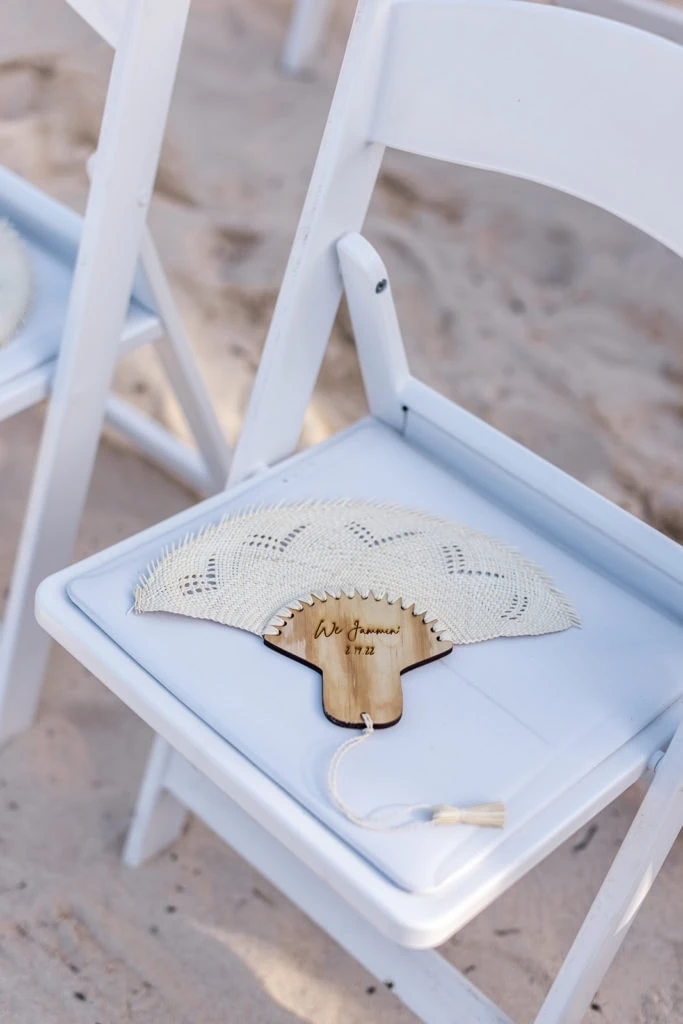 A macrame fan sits on a guest's chair at a beach wedding