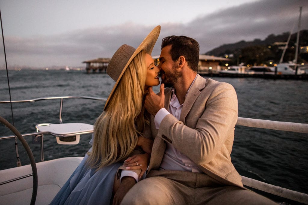 Couple kiss on sailboat during sunset engagement