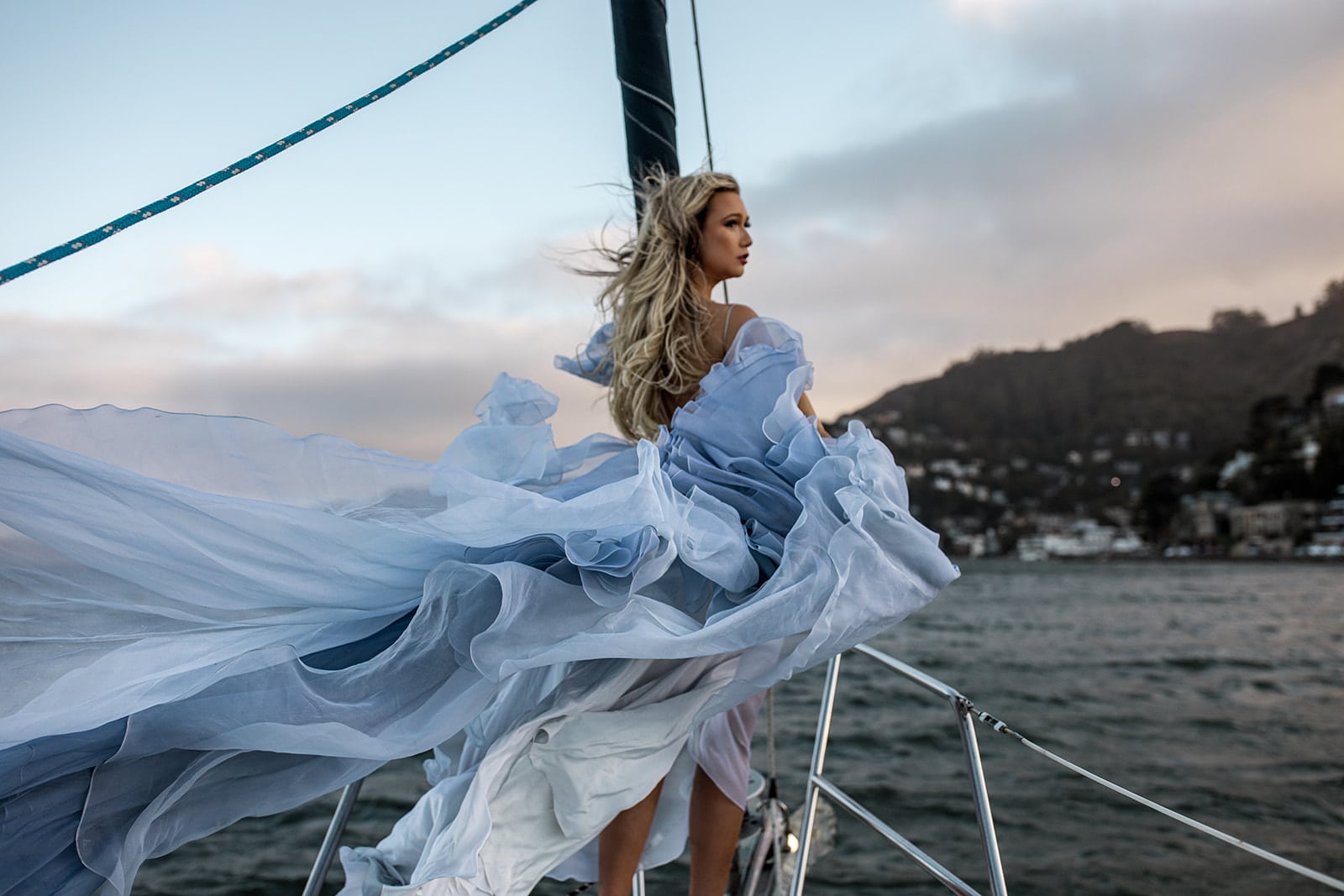 Woman stands on sailboat in flowy blue gown