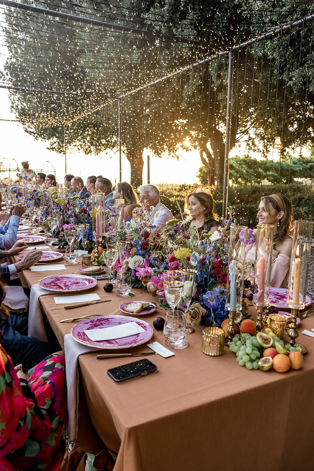 Guests sit at banquet style table in Tuscany Italy for wedding anniversary reception