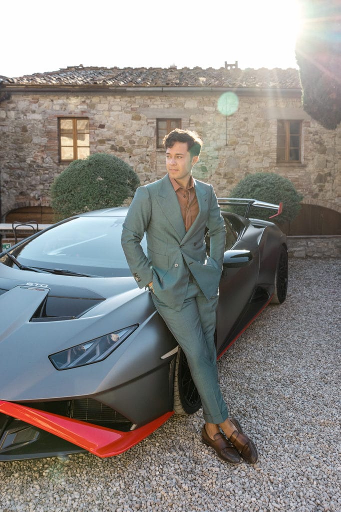 Man in custom suit blue suit, after finding groom's suit ideas, leans against Lamborghini
