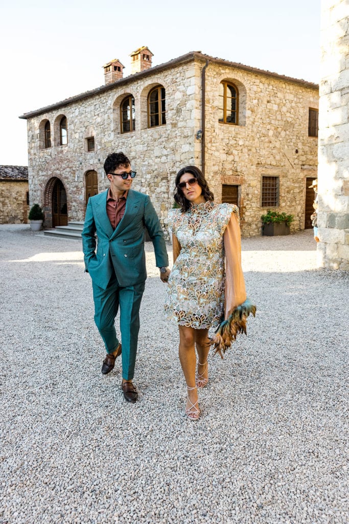Man, wearing groom suit ideas, and woman walk outside castello la leccia, tuscany italy