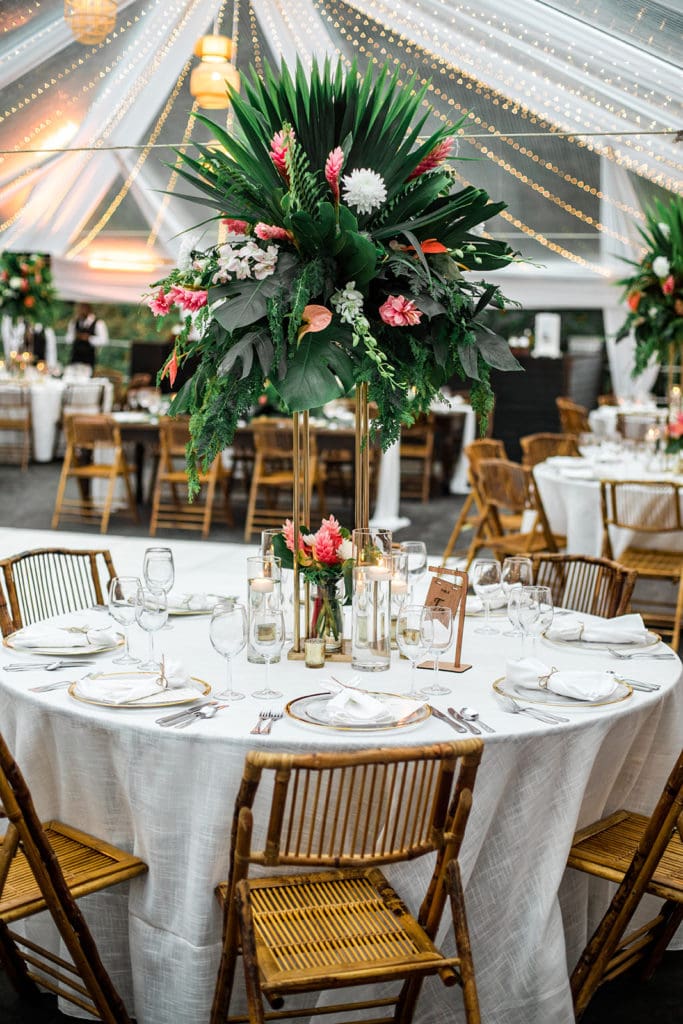 Large tropical floral arrangements are used as centerpieces at a tented wedding