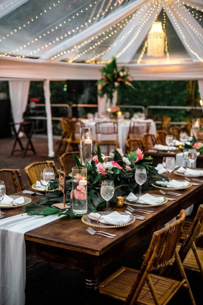 Pink and green floral centerpieces line a banquet-style table at a tented estate wedding
