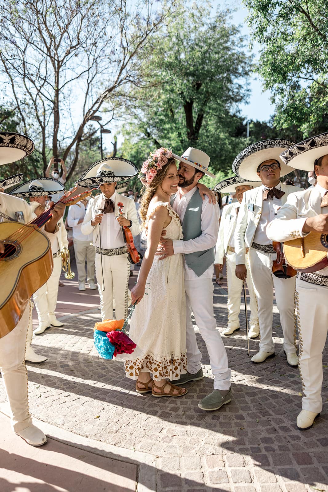 Bride and groom kiss while mariachi band plays in a park