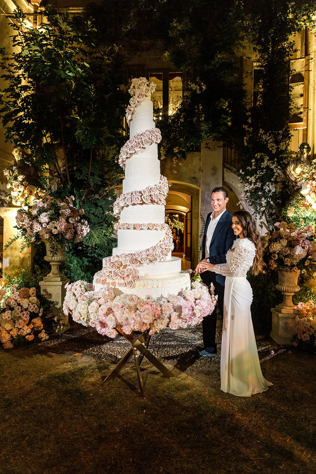 Bride and groom stand next to massive, 11-tiered wedding cake