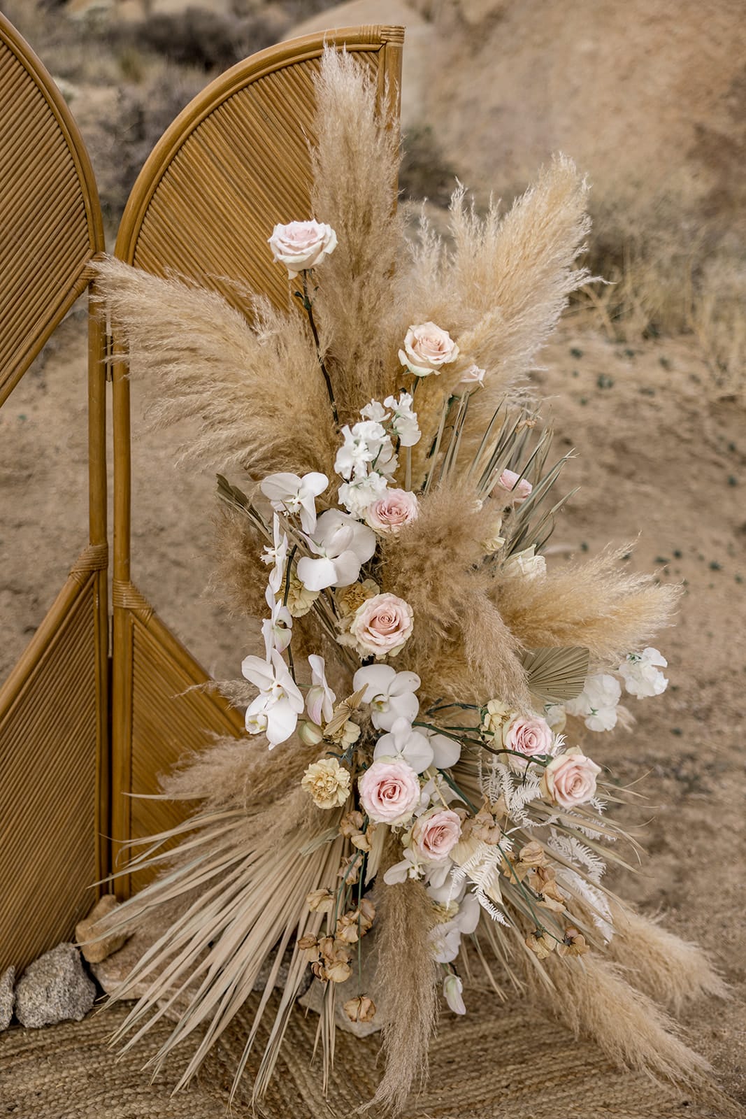 Pampas grass and pink and white colored roses adorn a wedding ceremony arch