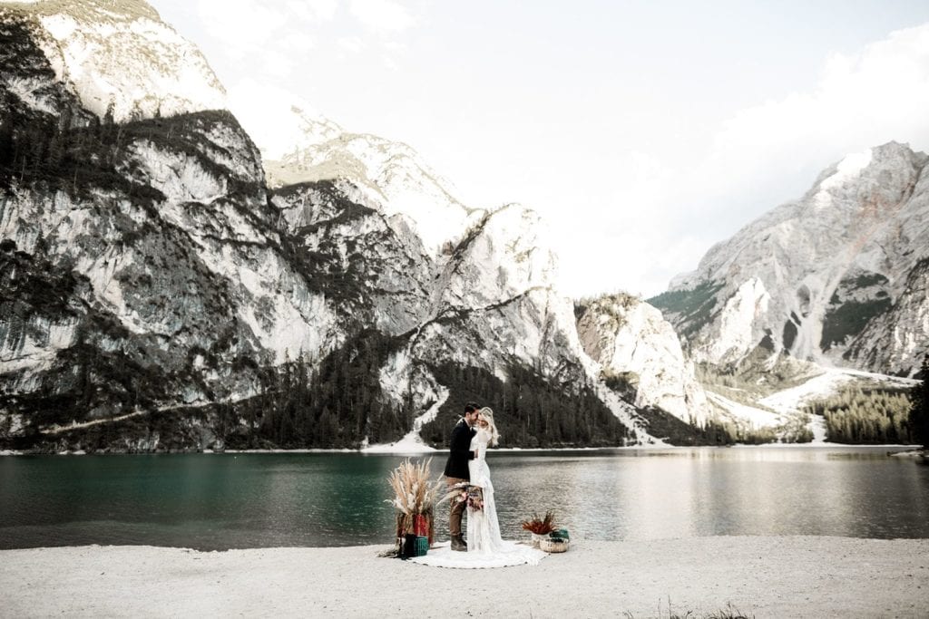 Man and woman share magical elopement in Dolomites in Italy with mountain peaks and lake in background