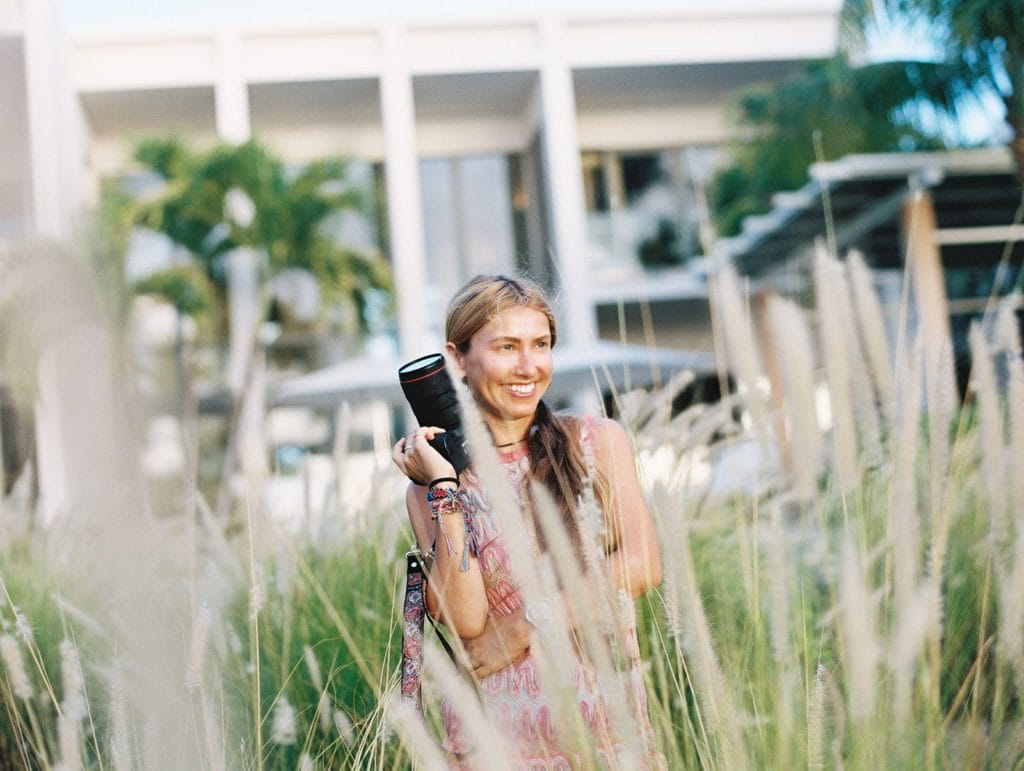 Picture of woman laughing, holding a camera, while photographing a beach destination wedding