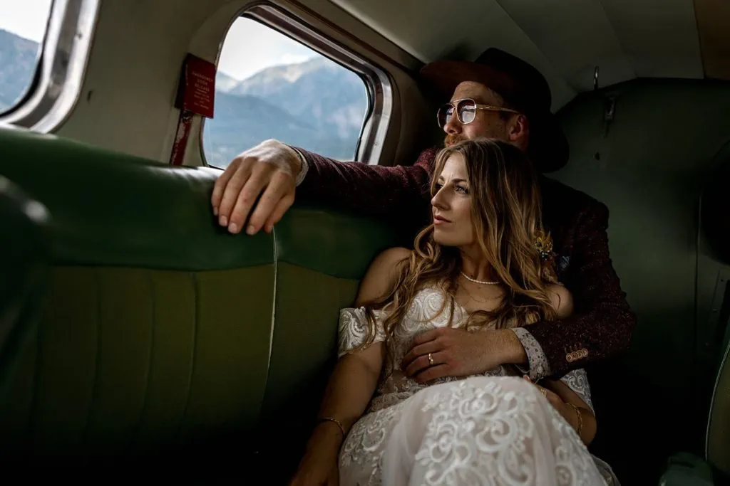 Bride and groom cuddle during a first flight in a vintage airplane after their wedding ceremony