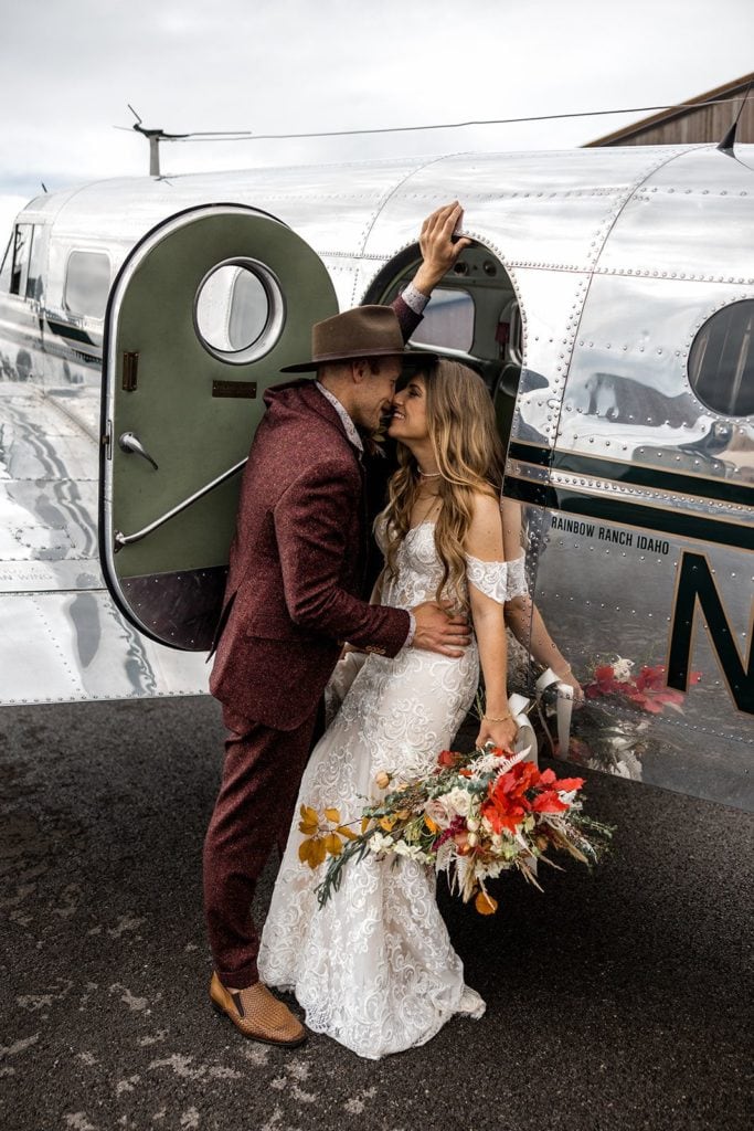 Bride and groom kiss during couple's portraits next to a vintage airplane