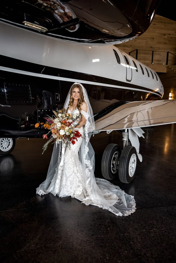 Bride holds bouquet next to vintage airplane for bridal portrait