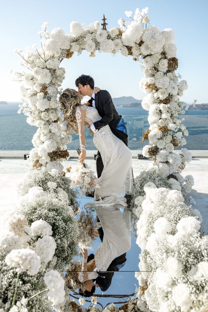 Bride and groom kiss under floral arch after Santorini wedding ceremony