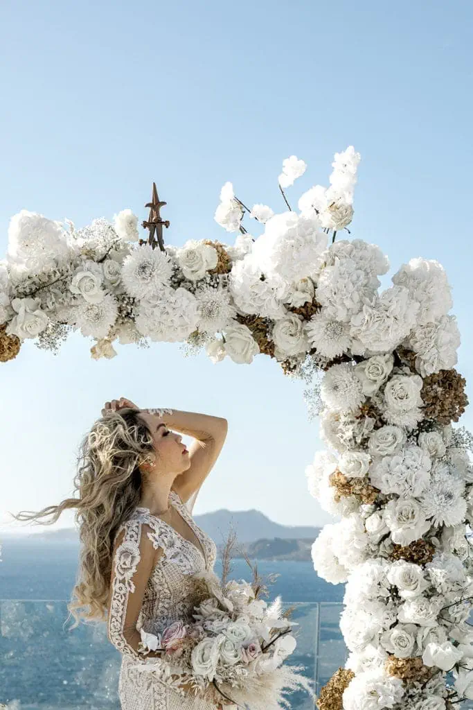 Bride stands in front of white floral arch after Santorini wedding