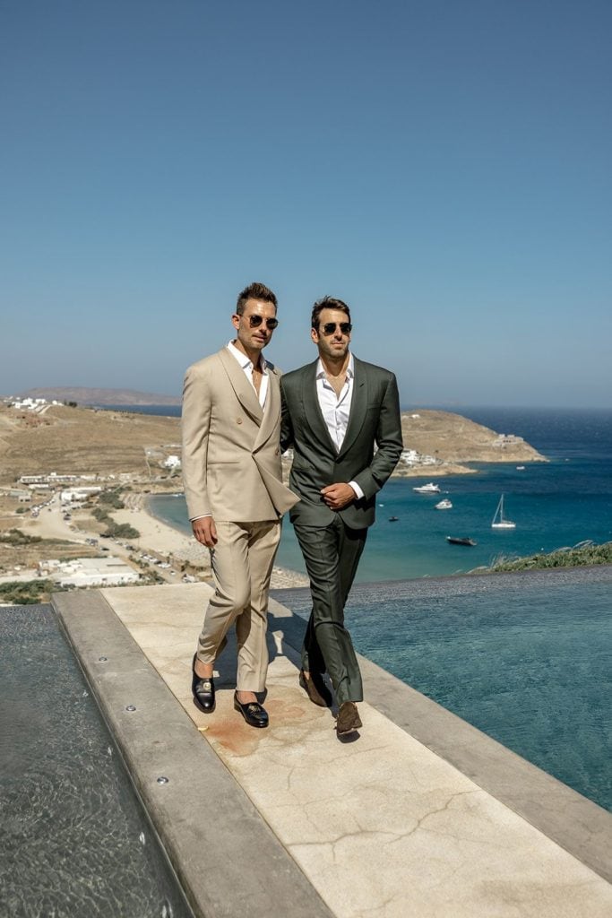 Grooms, both wearing beach wedding tuxedo ideas, walk to ceremony site together
