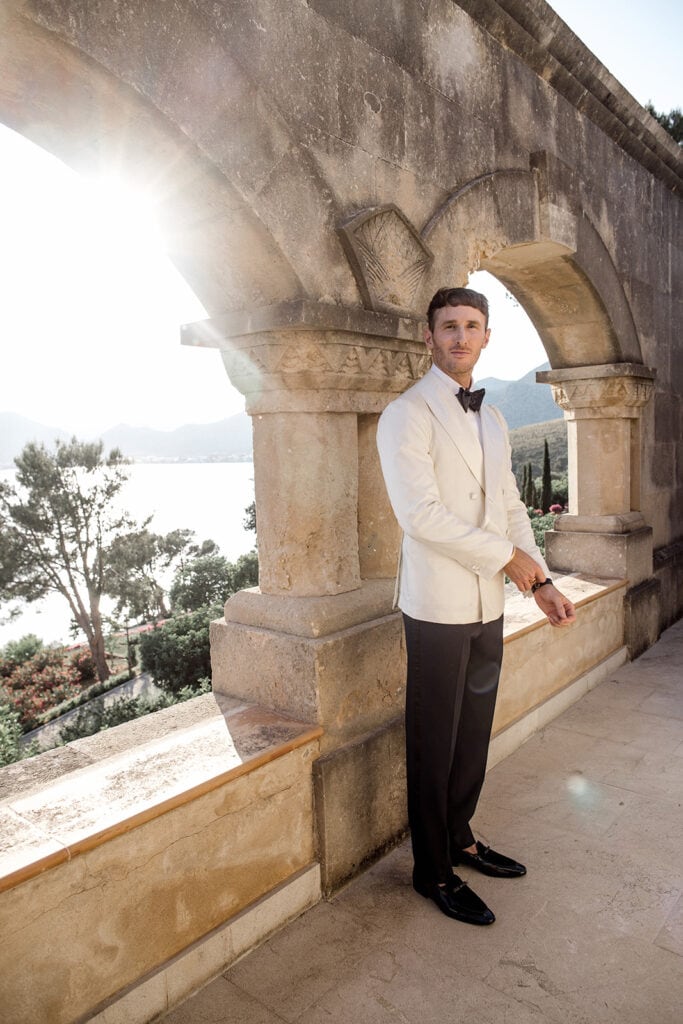 Groom wears white tuxedo jacket with black pants and black bow tie