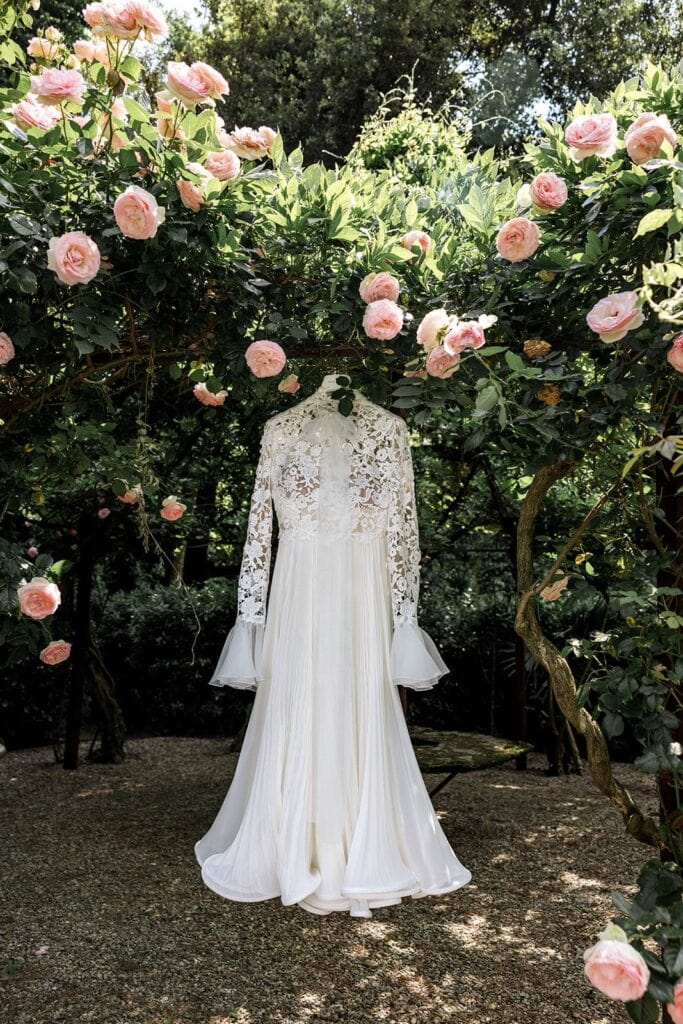 Bride's lace wedding gown hangs in garden for bridal detail portrait