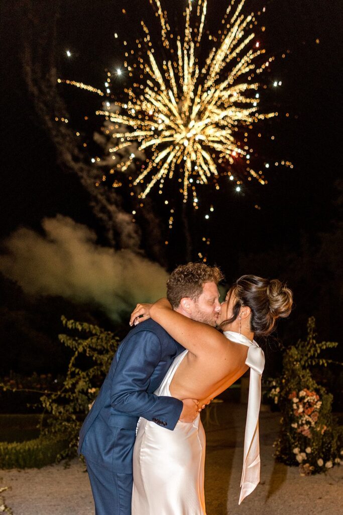Bride and groom kiss during reception fireworks
